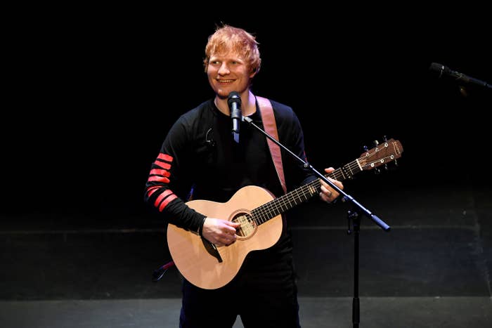 Ed Sheeran smiles on stage while strumming a guitar