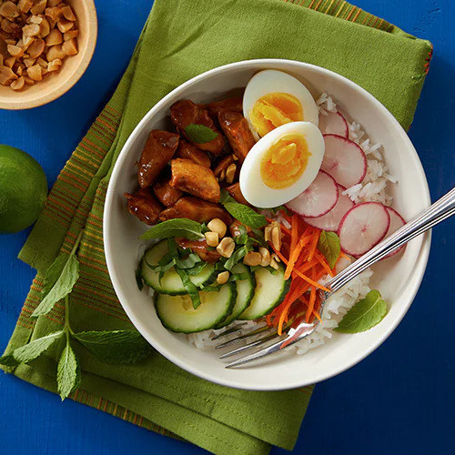 rice bowl topped with sliced cucumber, radish, carrots, chicken and hard boiled egg