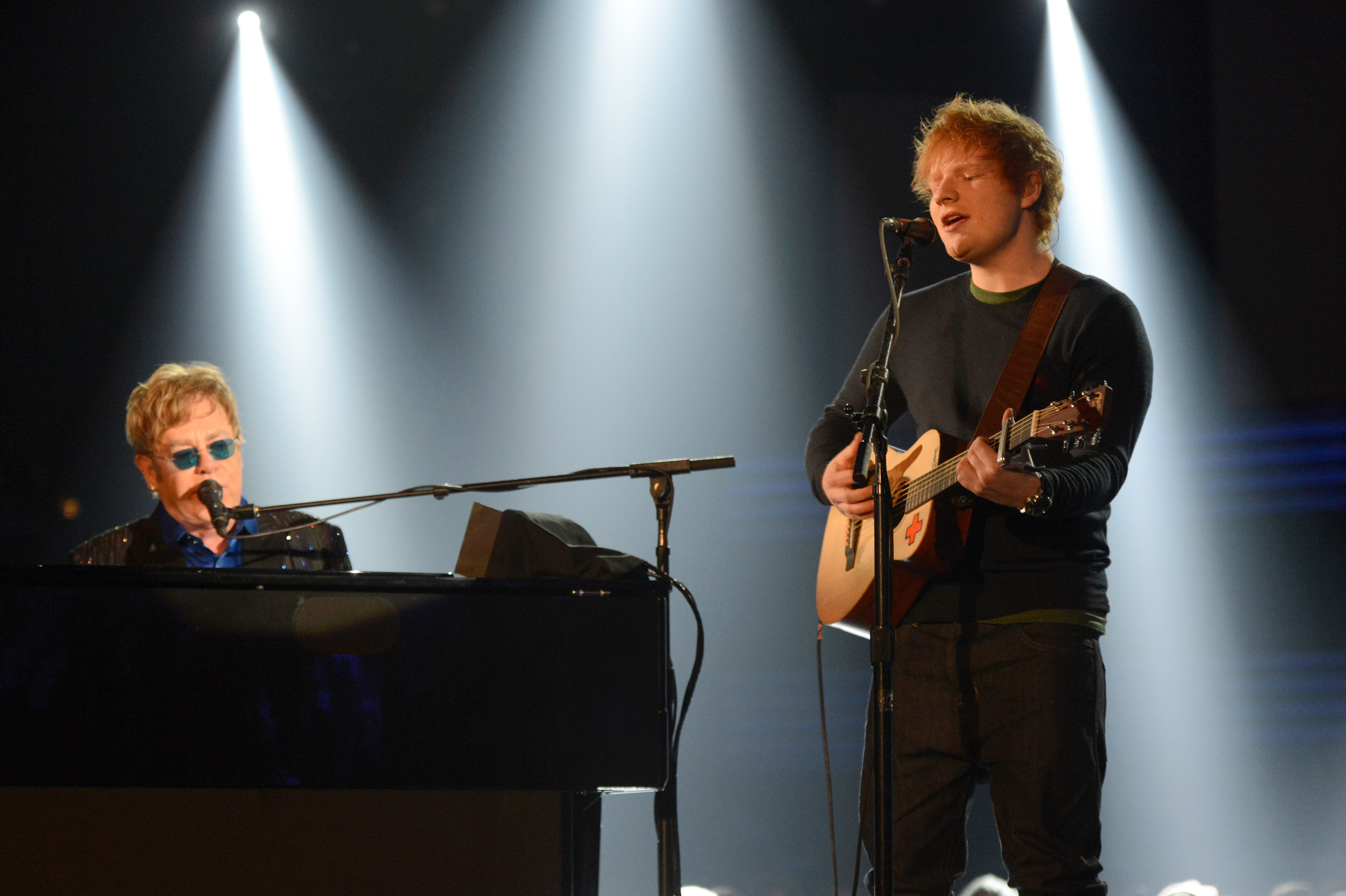 Sheeran sings with a guitar in hand as John plays the piano