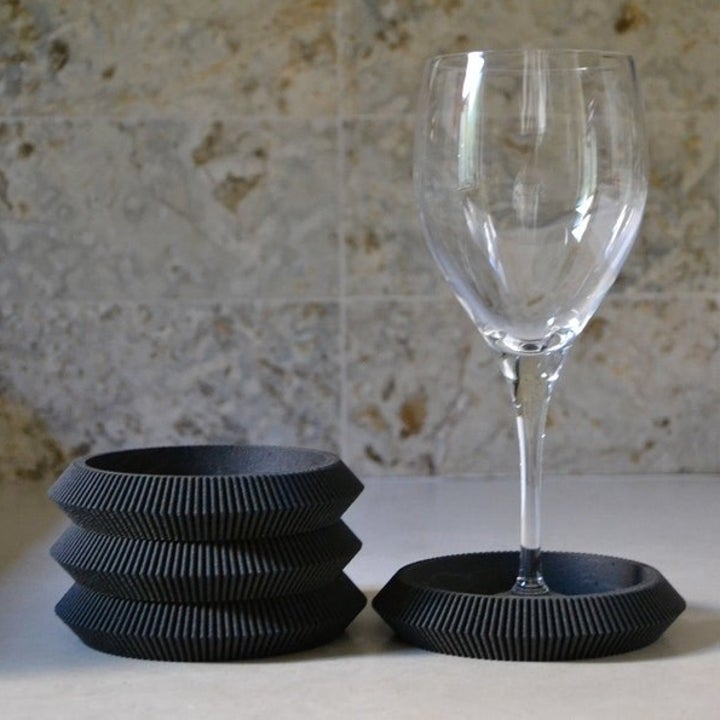 three black coaster stacked and one on the side with a wine glass on top