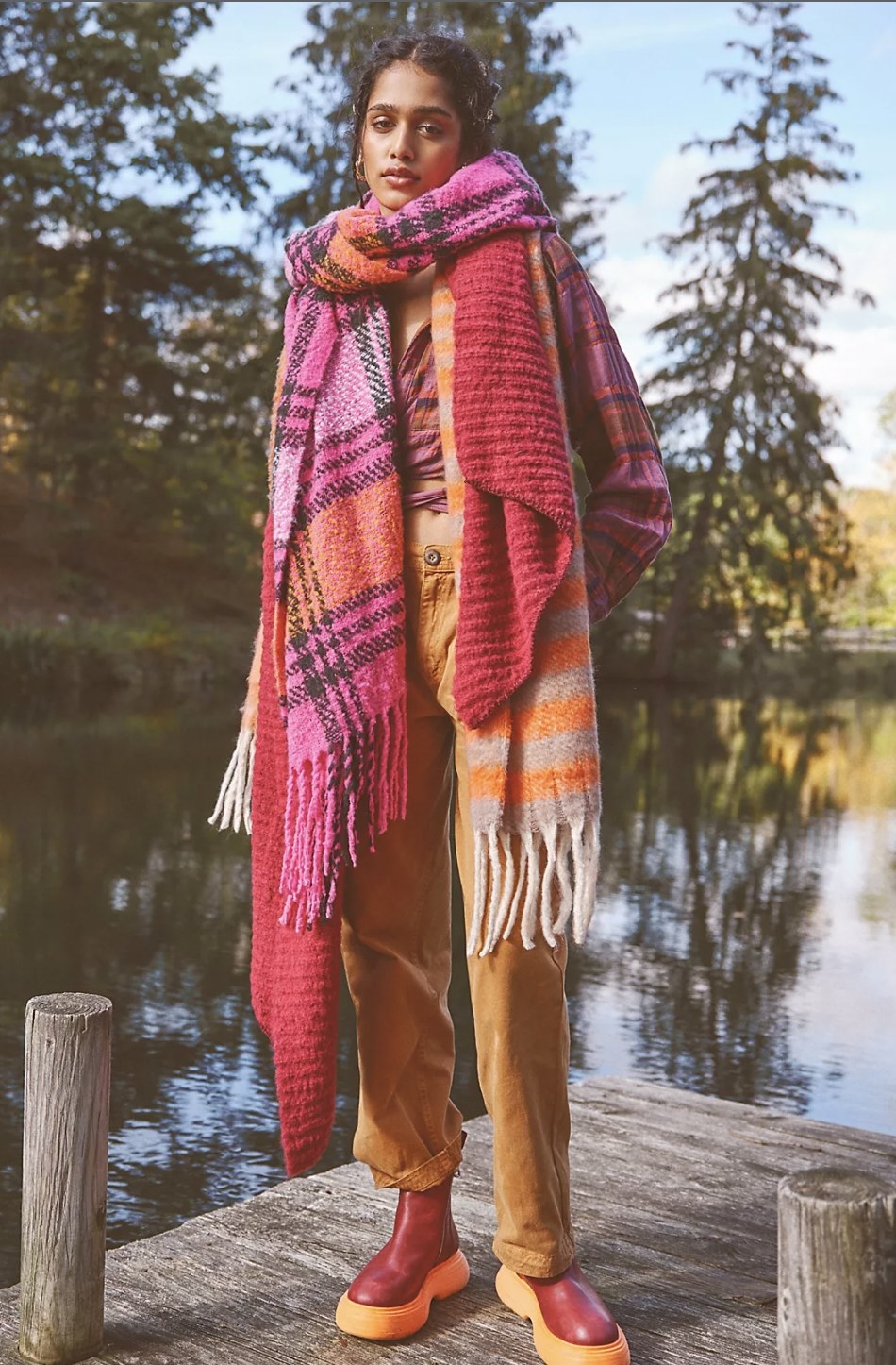 Model wearing the pink plaid scarf draped over her neck and tied once, with fringed edges hanging down