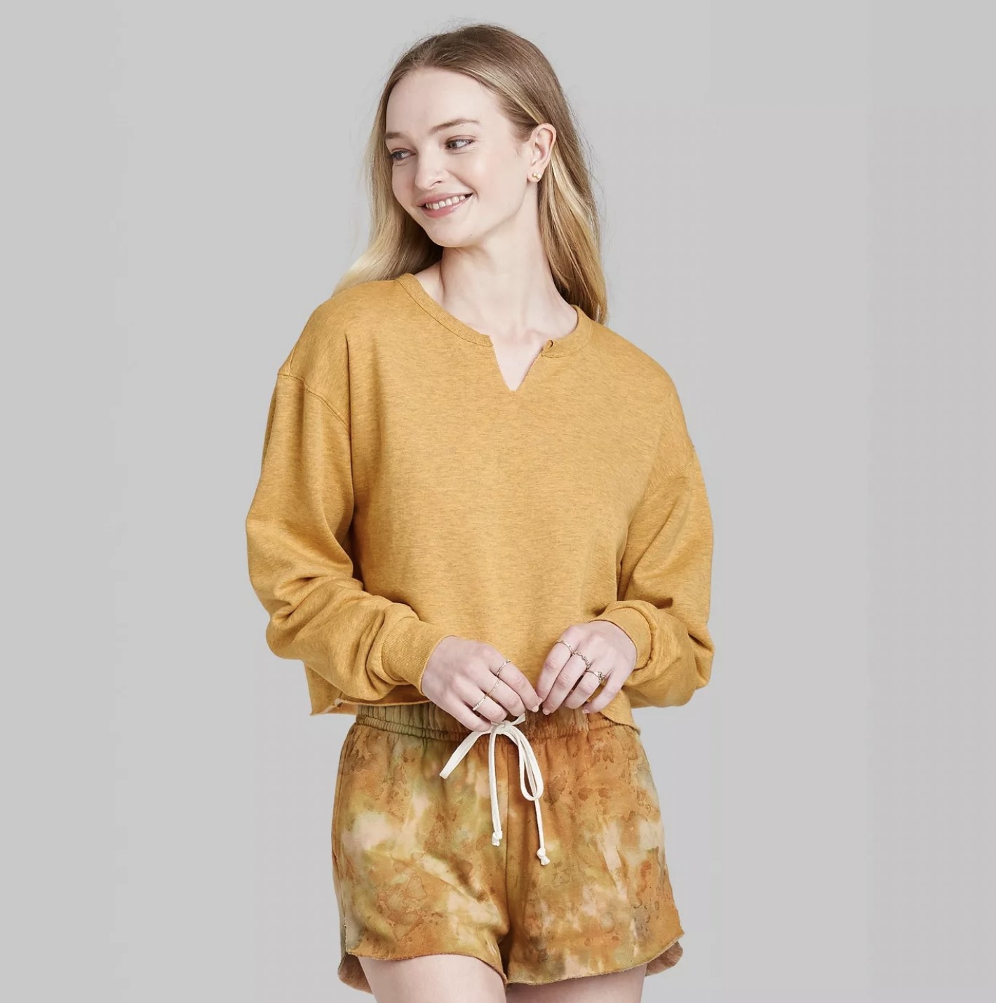 Model in the mustard sweatshirt style top and tie-dye shorts