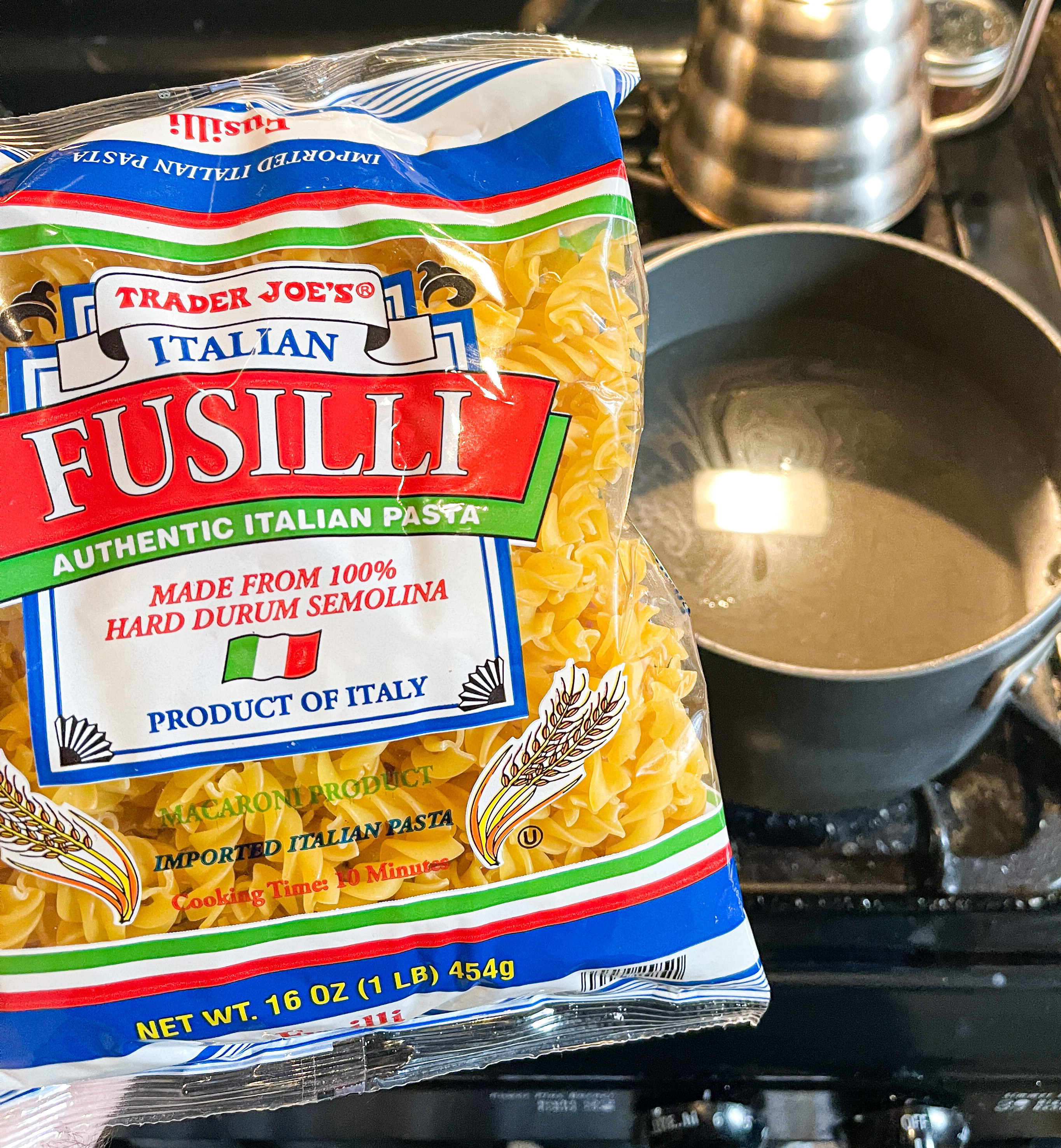 Package of fusilli pasta next to a pot of water on the stove