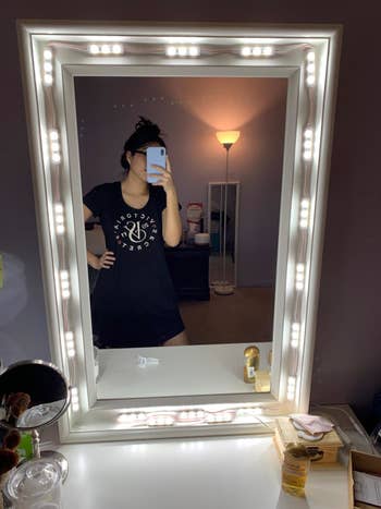 A reviewer's photo of themselves reflected in the vanity mirror with light strips around the side