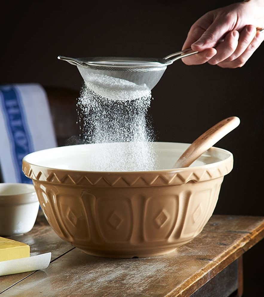 A hand sifting flour into the beige bowl