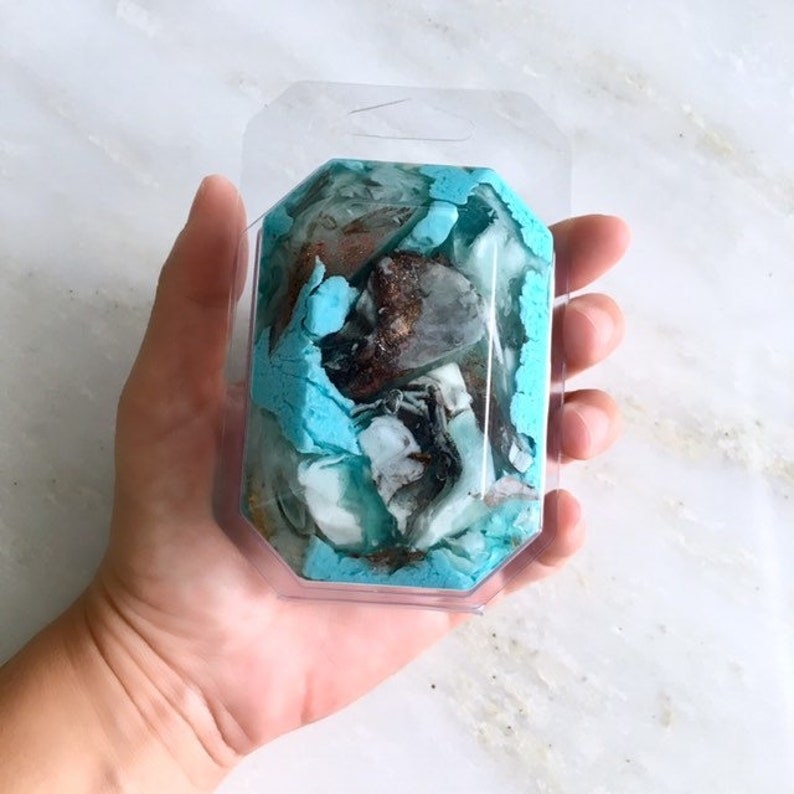 hand holding a gemstone-shaped boar of soap in blue and black iridescent