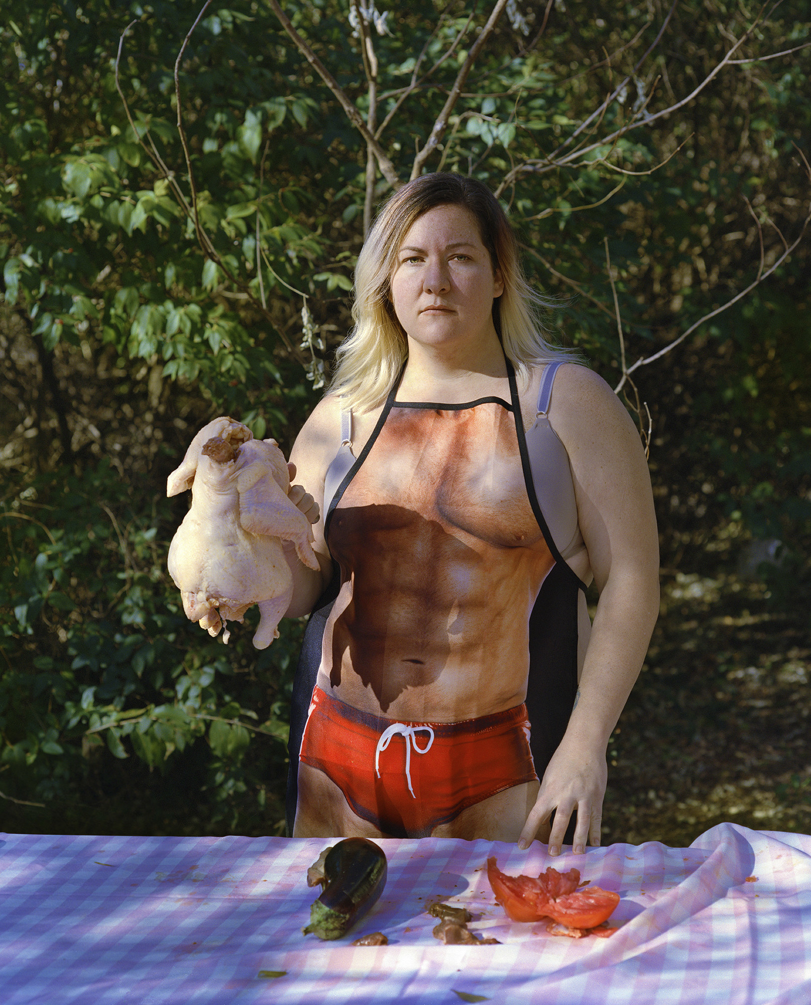 a person stands holding a chicken wearing an apron of a man&#x27;s naked body 