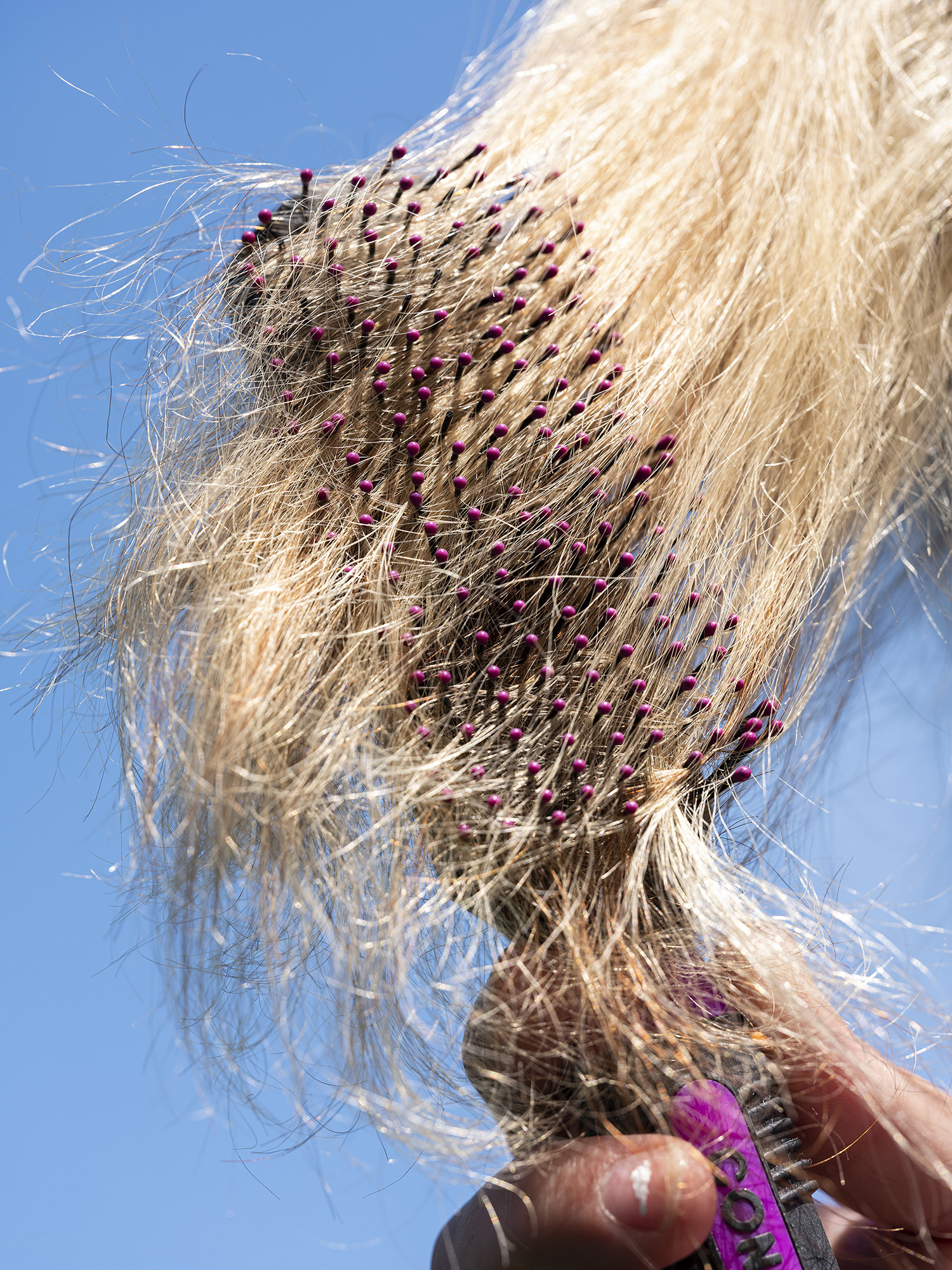 a hairbrush pulls through long blonde hair against a sky background 