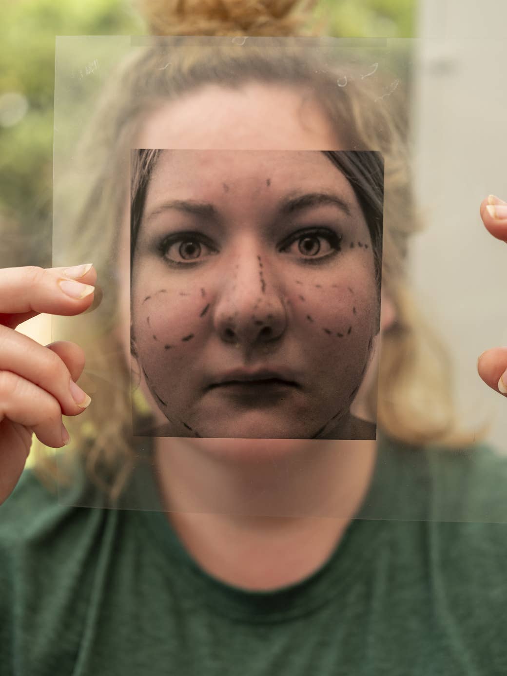 a person in a t shirt holds a negative of their face with lines on it in front of their face with two fingers