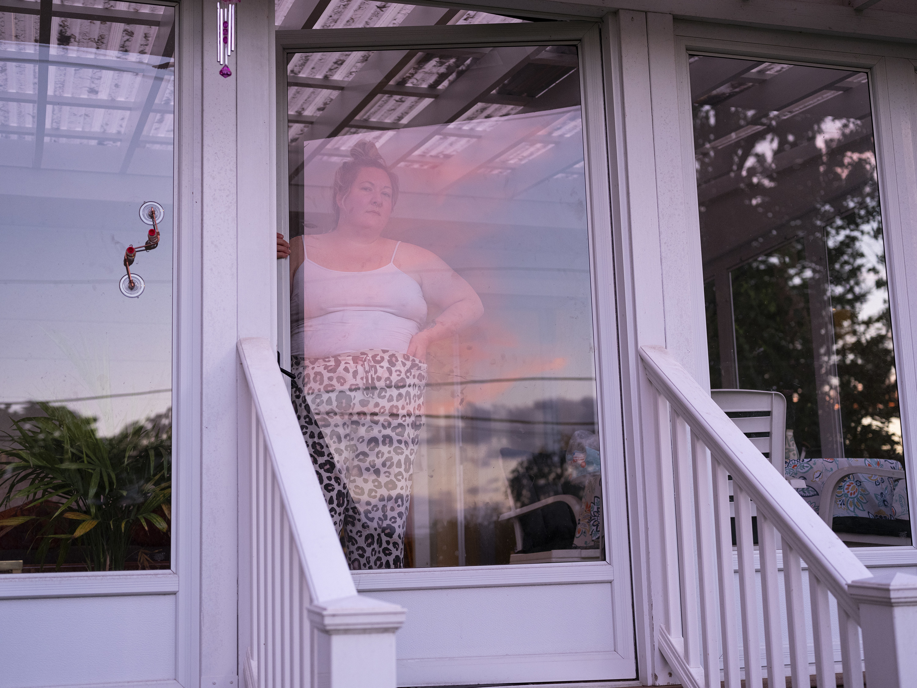 a person in a tank top and leopard print pants stands in front of a glass door entrance to a home 