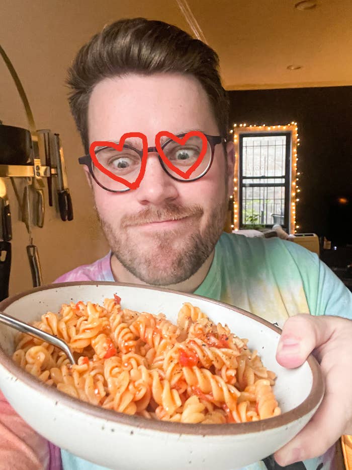 Author holding a bowl of pasta with marinara sauce with drawn-on heart eyes