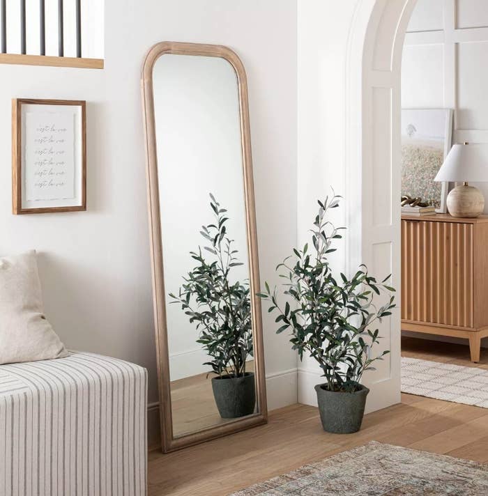 Leaning floor mirror with wooden frame, on wooden floor next to potted plant