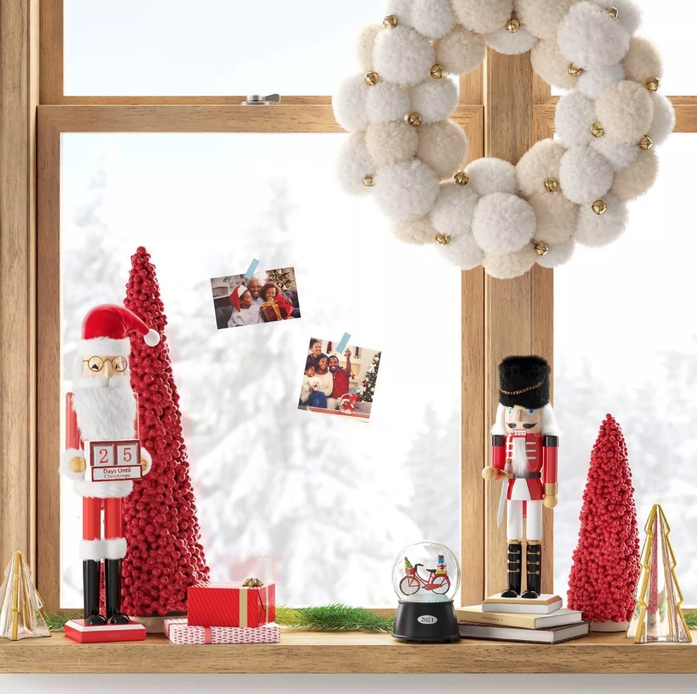 Beige and white pom pom wreath on window above nutcracker decoration display on wooden window sill