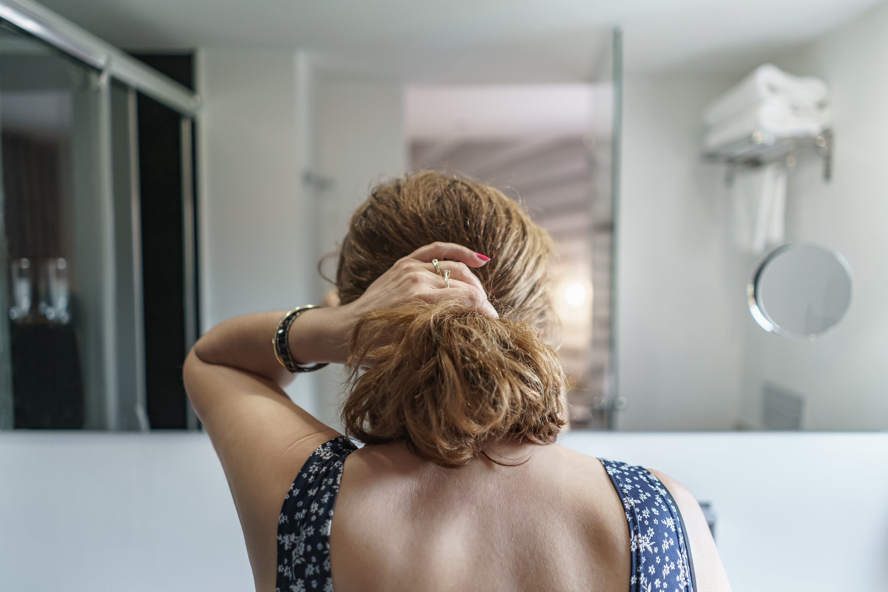 The back of a girl&#x27;s head and her hand is holding her hair in a ponytail