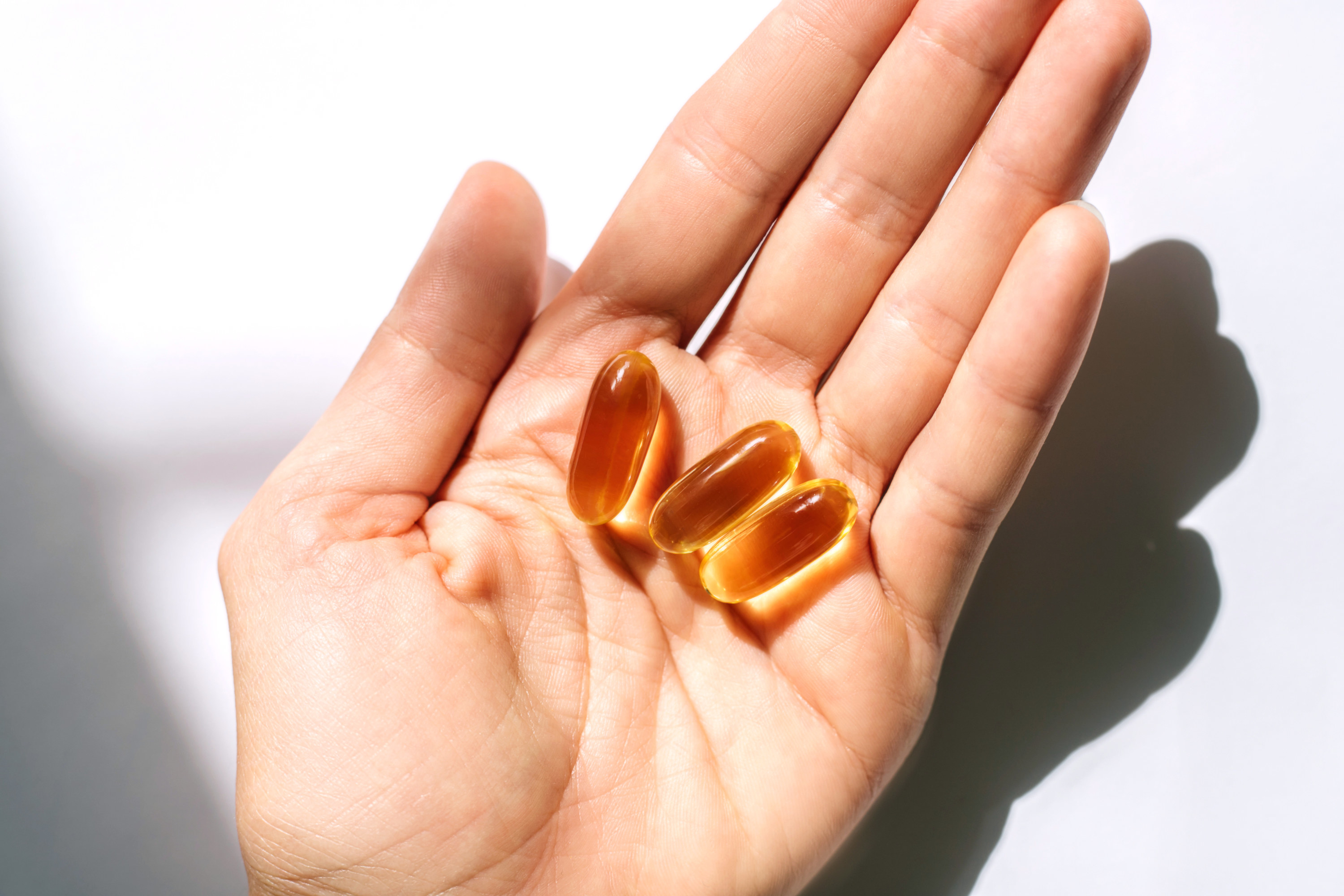 A hand with three vitamin capsules in it