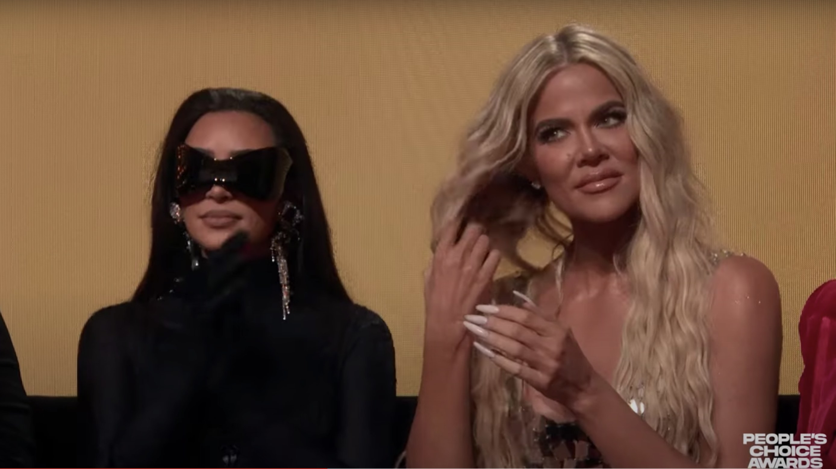 Khloe flips her hair while sitting in the audience while Halle speaks on stage