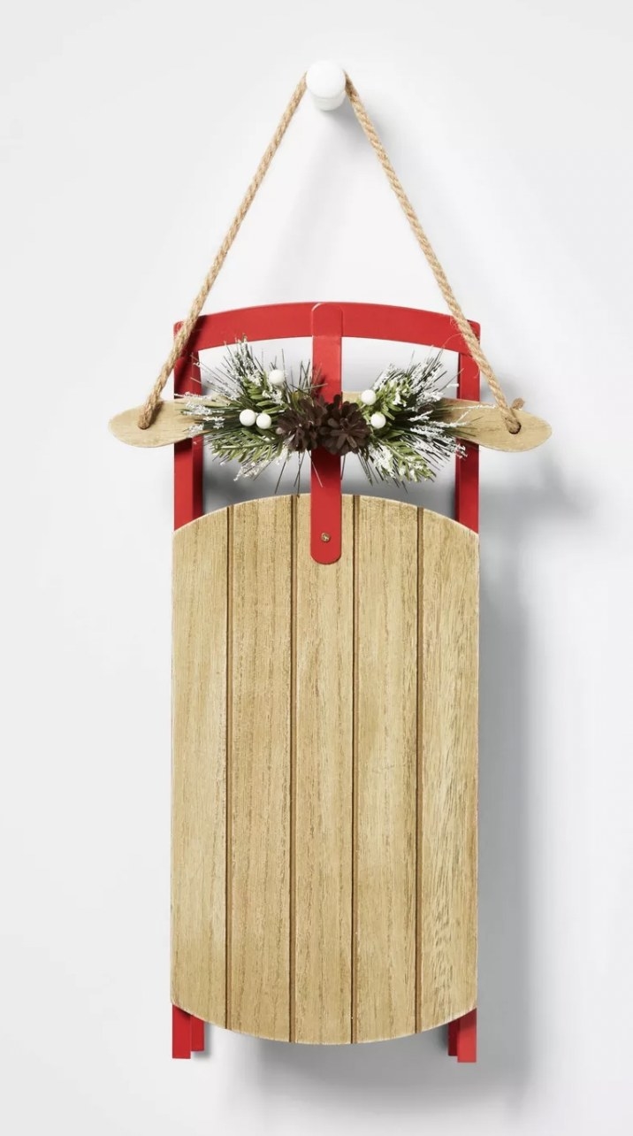 a mini sleigh adorned with greenery hanging on a wall