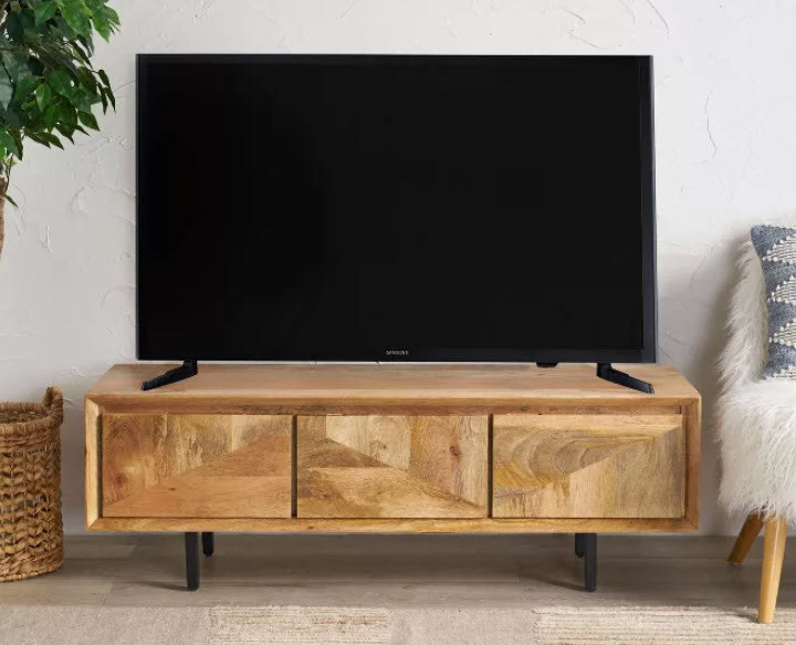 A tan mango wooden TV stand with 3 doors and smooth black metal legs. Wood has a unique design on the doors and the stand can hold up to 54&#x27;