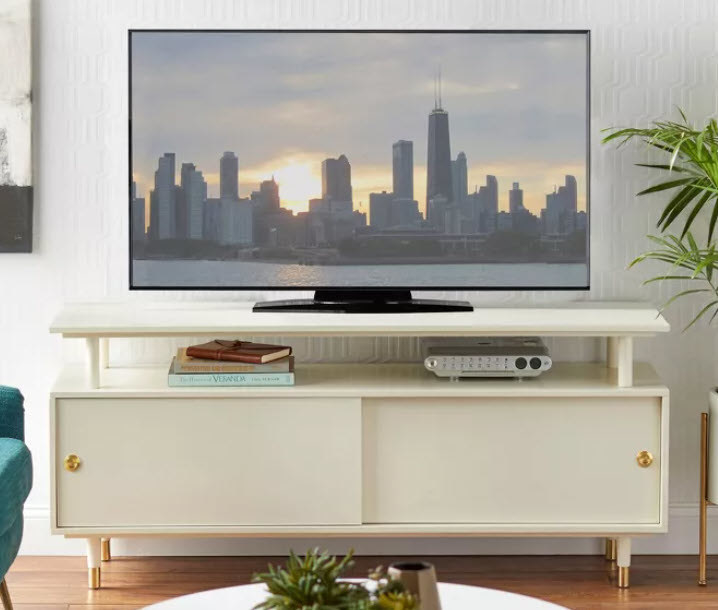 An all white TV stand with gold accents on the handles and tapered legs. Open middle shelf under main TV stand for more storage.