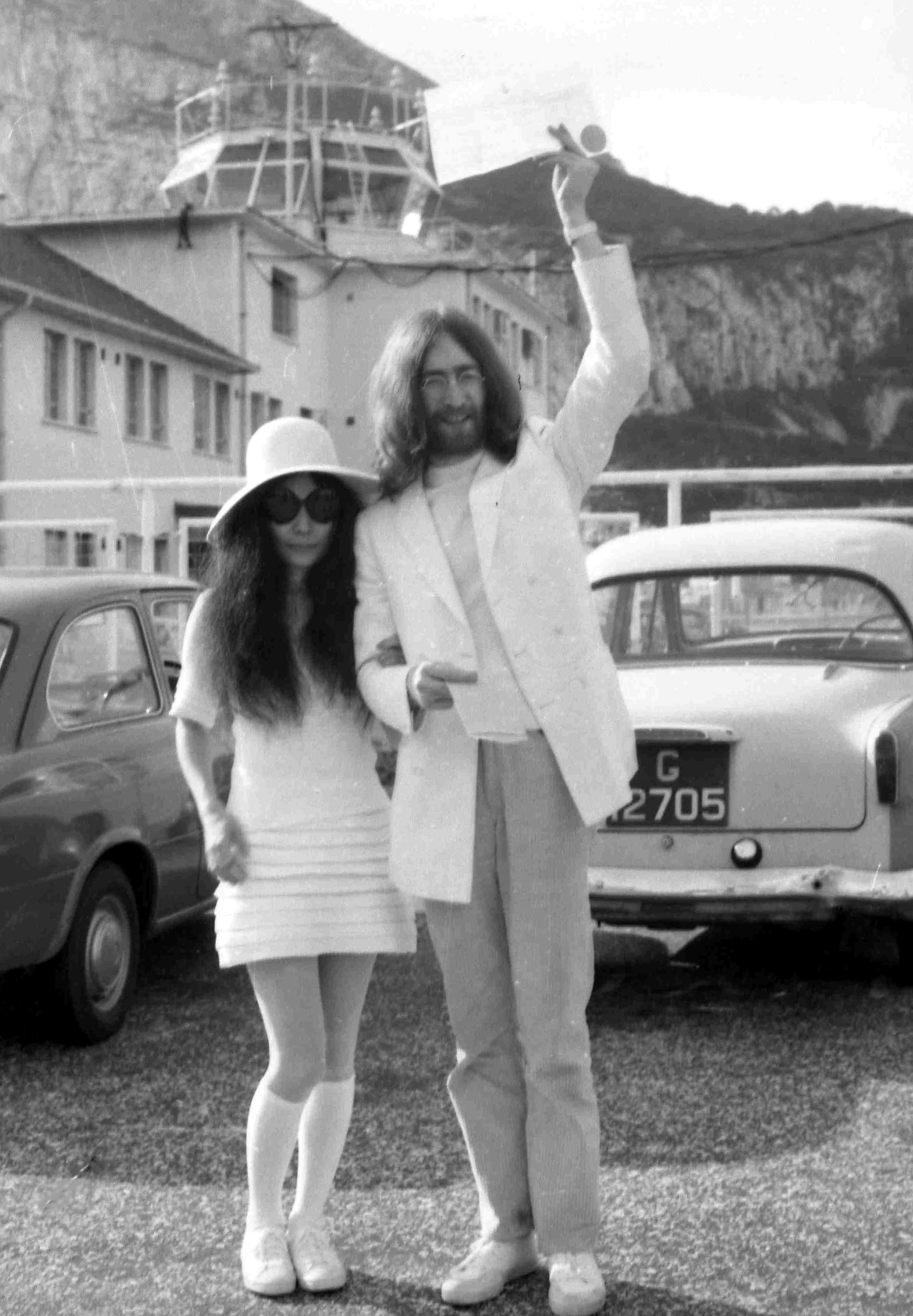 John Lennon and Yoko Ono  at their wedding in a parking lot with two cars behind them