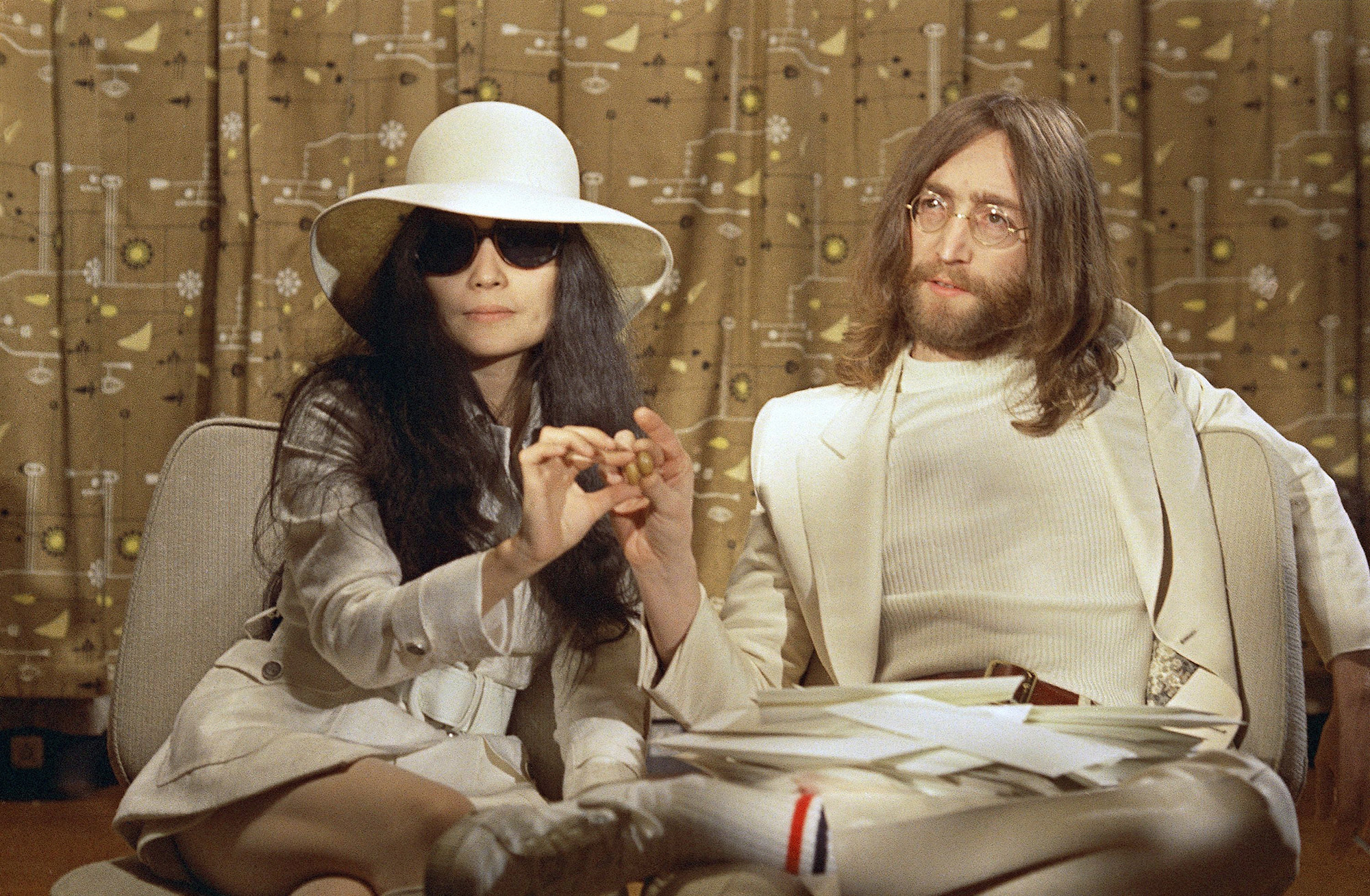 John Lennon and Yoko Ono  in beige sitting giving an interview and holding up olives to the camera