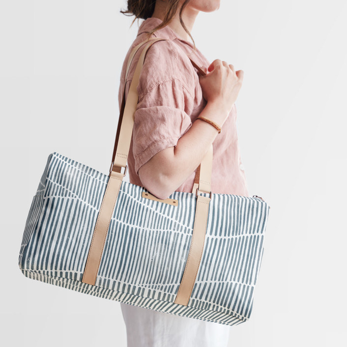 model holding the long round duffle in white with grey line pattern and light tan straps