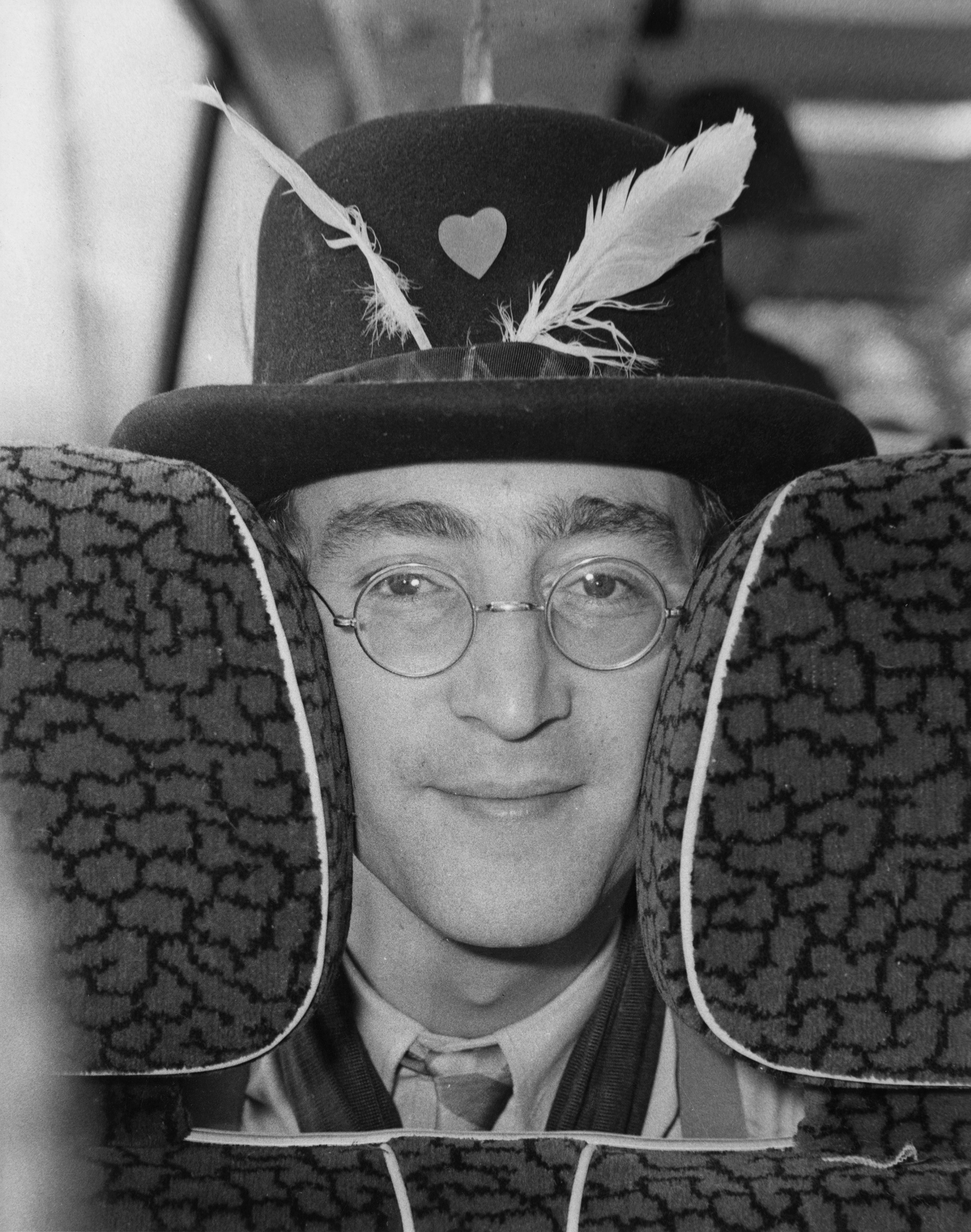 John Lennon with his face squished between two seat headrests wearing a hat with feathers