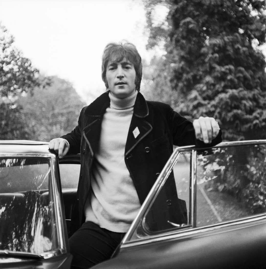 John lennon in a shearling jacket looking at the camera on a country road half out of a car