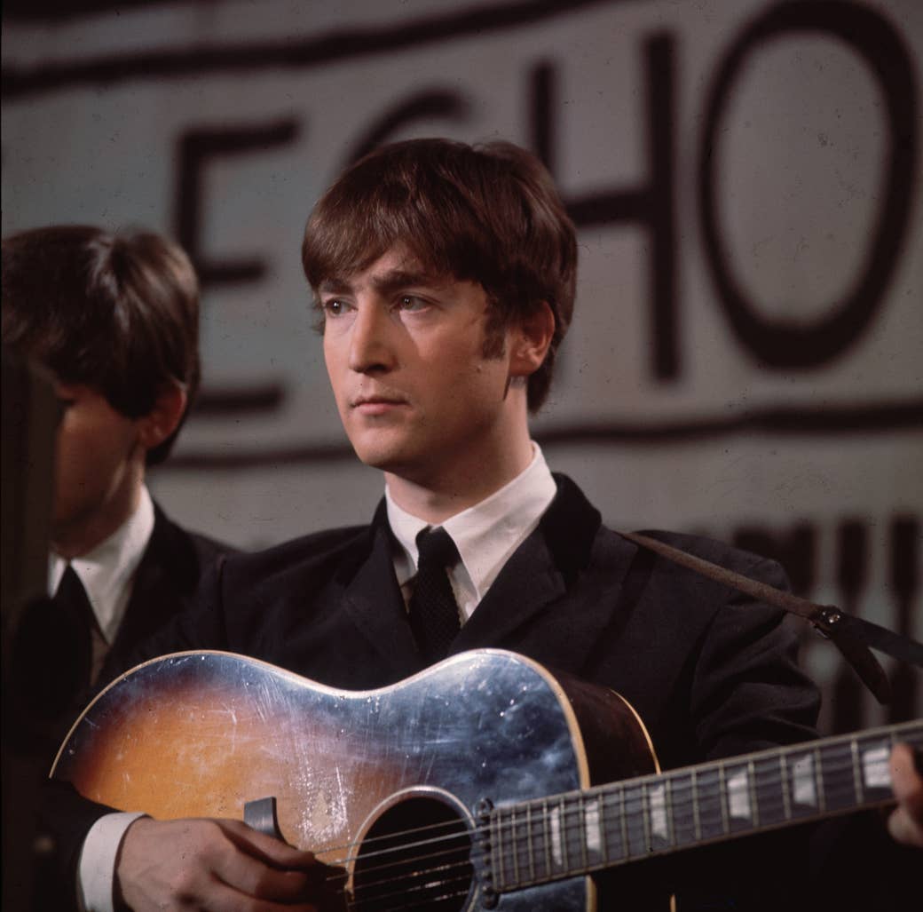 john lennon holding a guitar on stage in a suit