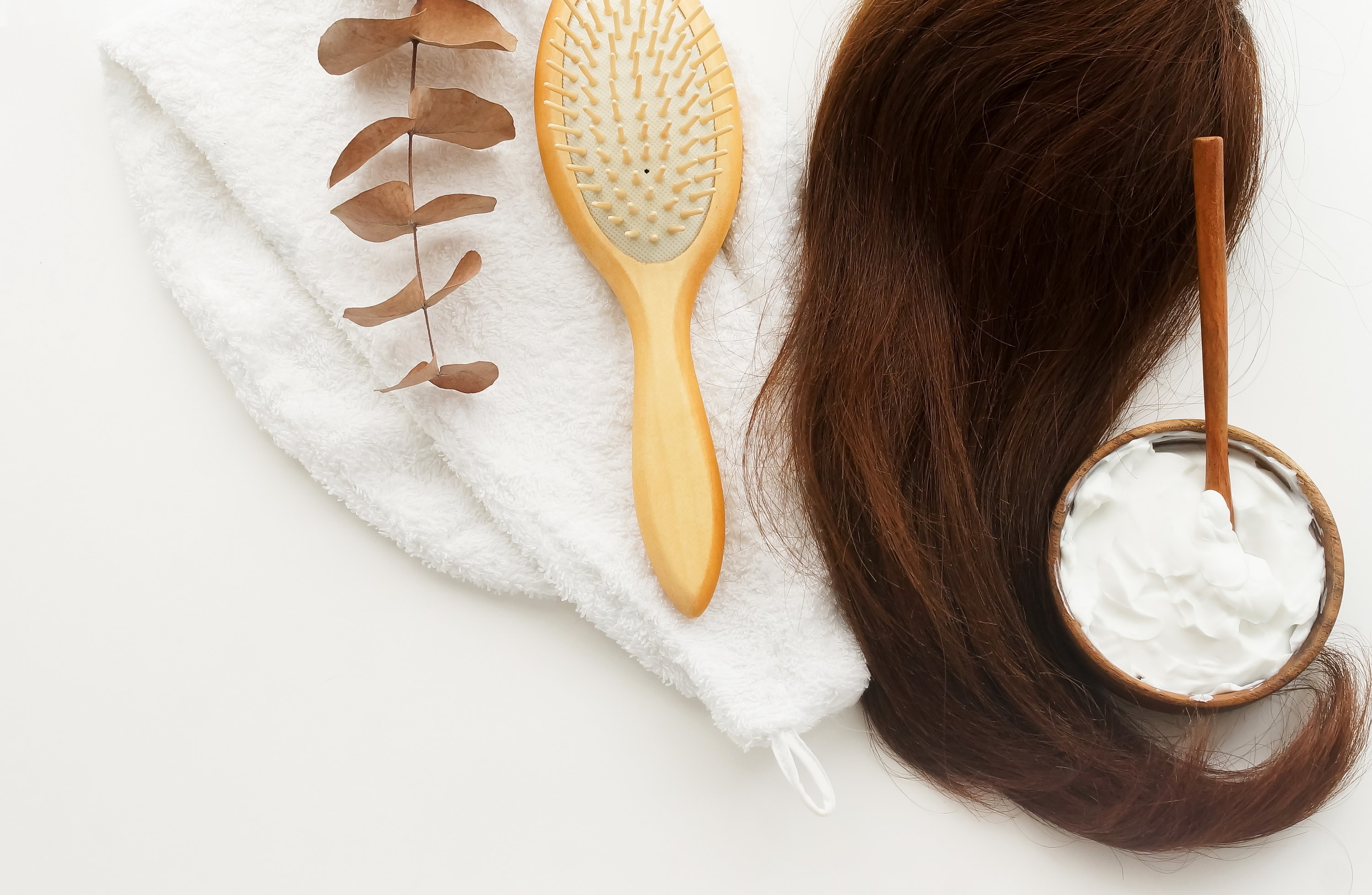 A brush, hair, and a bowl of hair mask laying on a white towel
