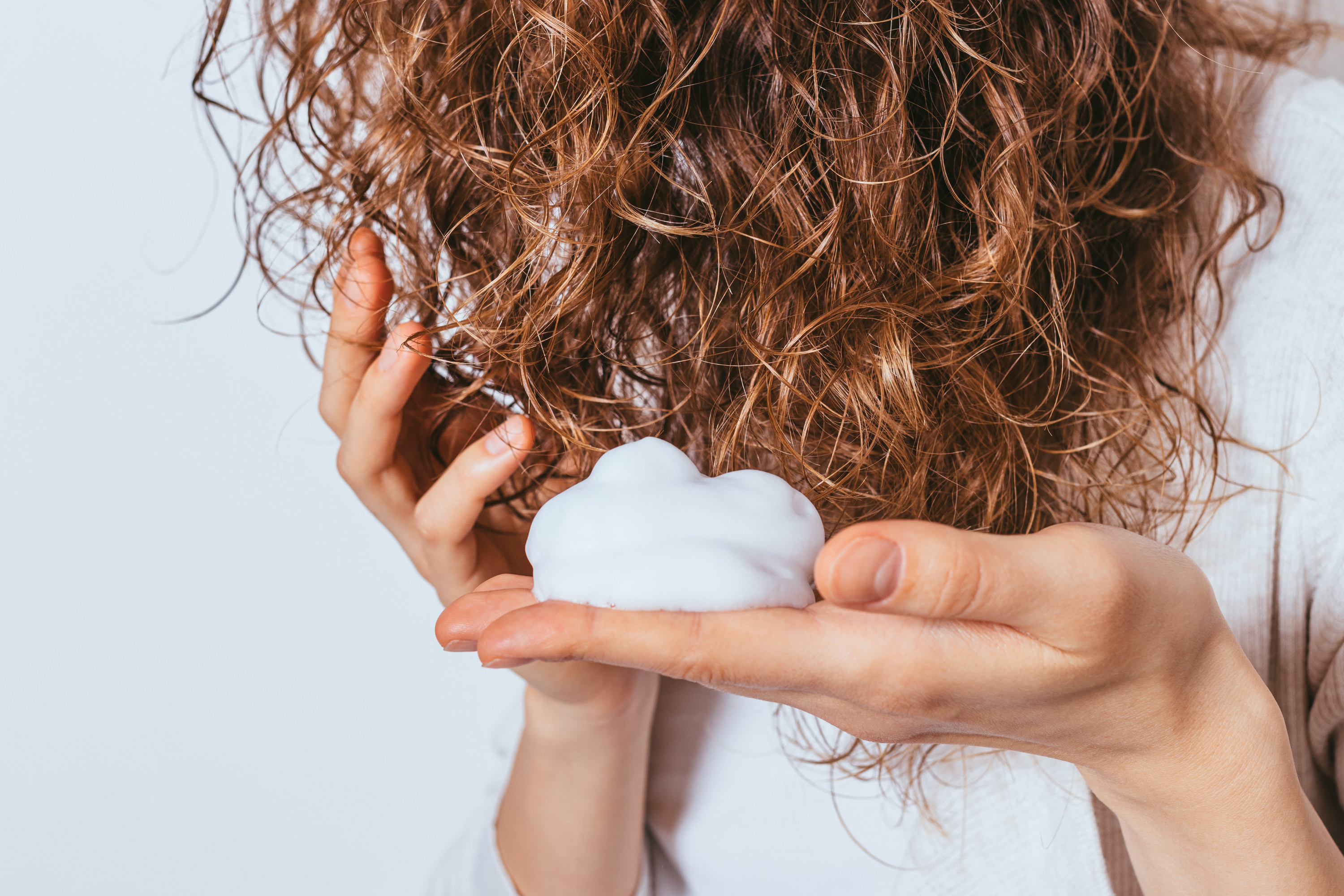 A dollop of hair product in the palm of a hand being put into hair