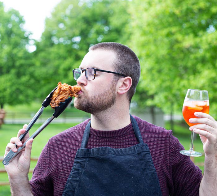 Author jokingly kissing a piece of fried chicken while cooking, and holding a cocktail