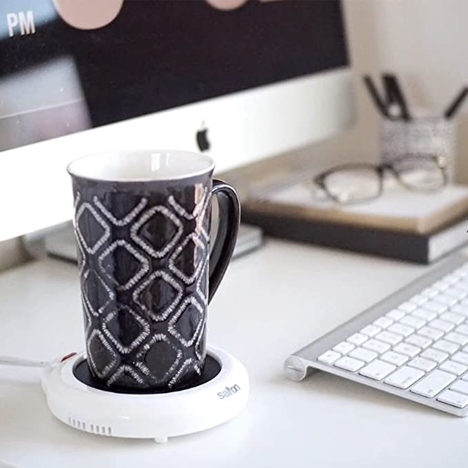 A coffee mug sitting in a mug warmer on top of a desk