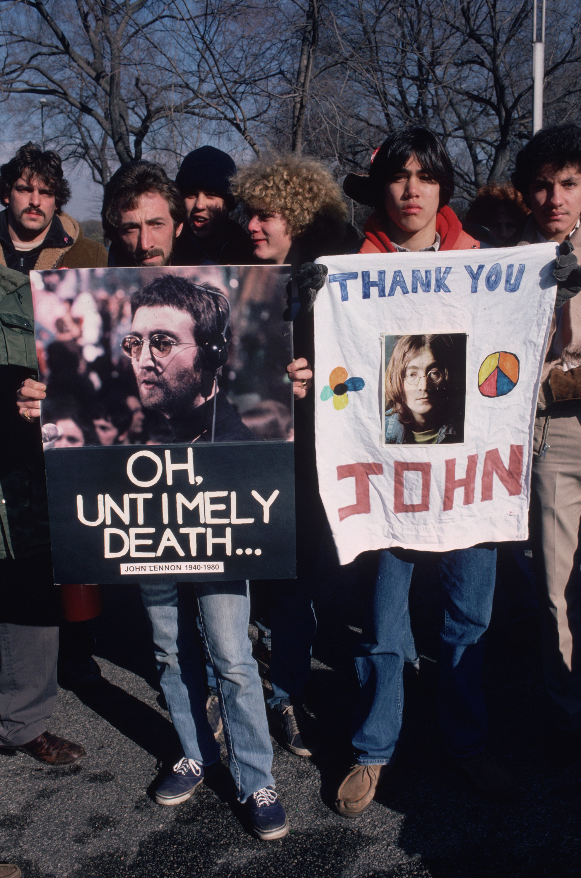 People in a crowd holding signs that say oh untimely death and thank you john after the death of john lennon