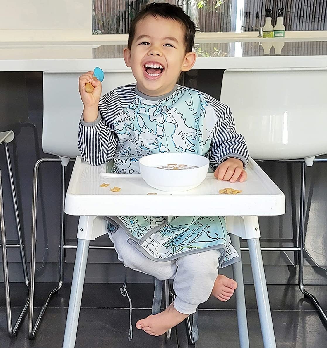 a child model wearing the long sleeve bib while siting in a high chair