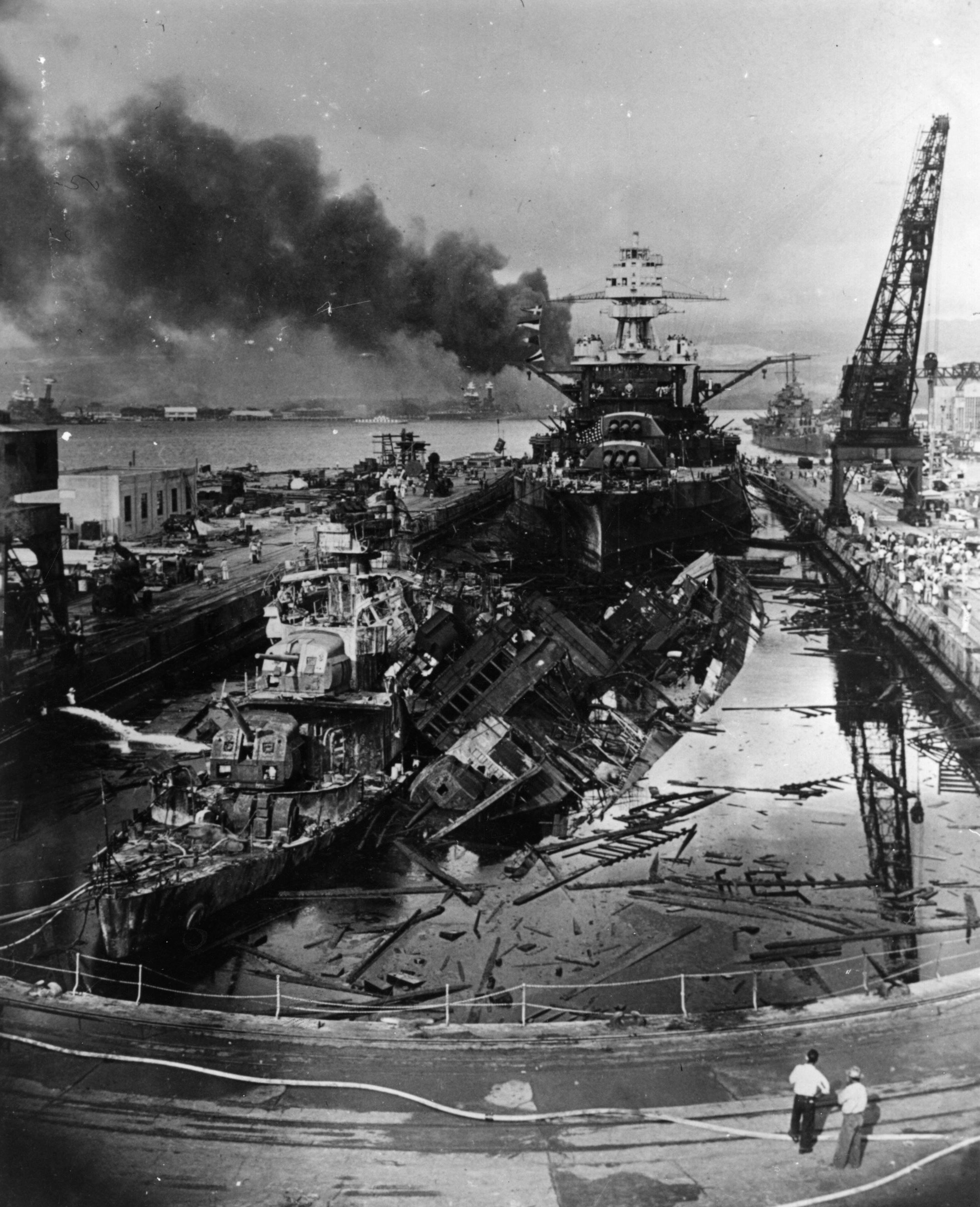 A destroyed battleship at Pearl Harbor as two onlookers stand bottom left 