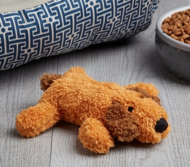 Brown plush dog toy next to bowl of dog food and dog bed