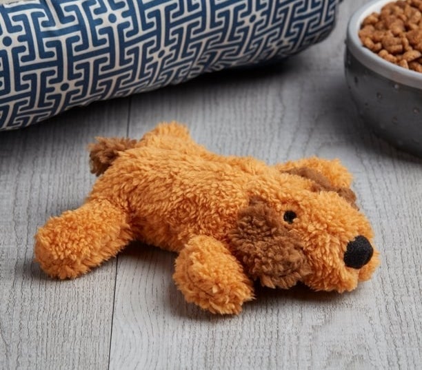 Brown plush dog toy next to bowl of dog food and dog bed