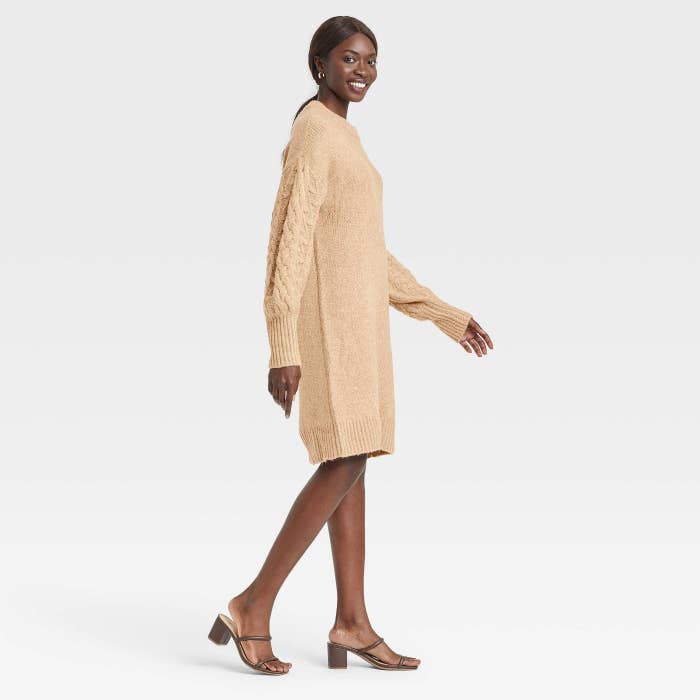 model in the knee length tan sweater dress with cables down the long sleeves