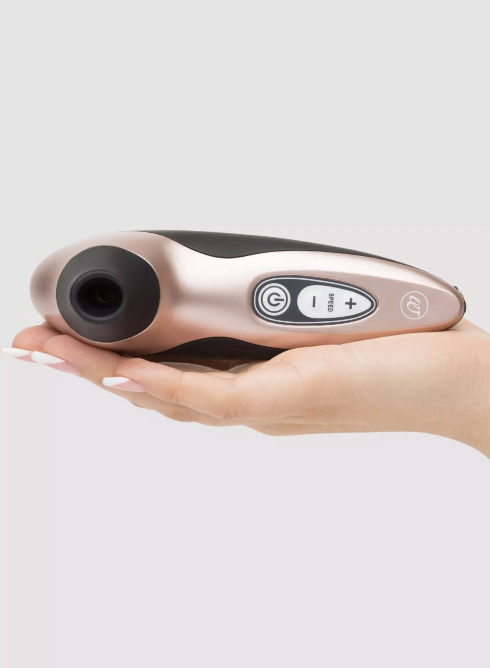 The pink stimulator resting in someone&#x27;s palm, showing the silicon-tipped suction area and control panel, with power button and - and + controls for speed