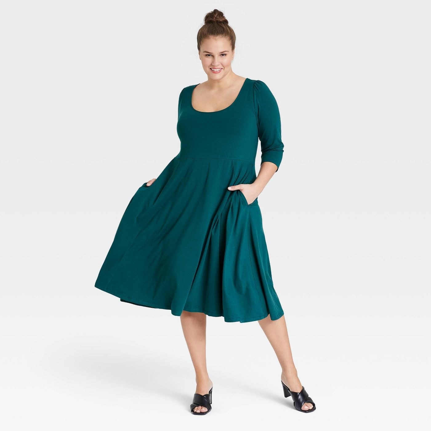 model in a teal round-neck midi dress with a flowy skirt and pockets