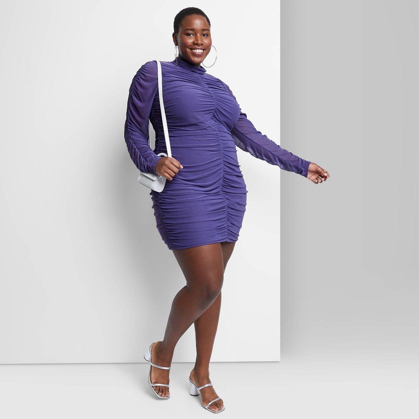 model in a purple mini long sleeve dress with ruching up the front and on the sleeves