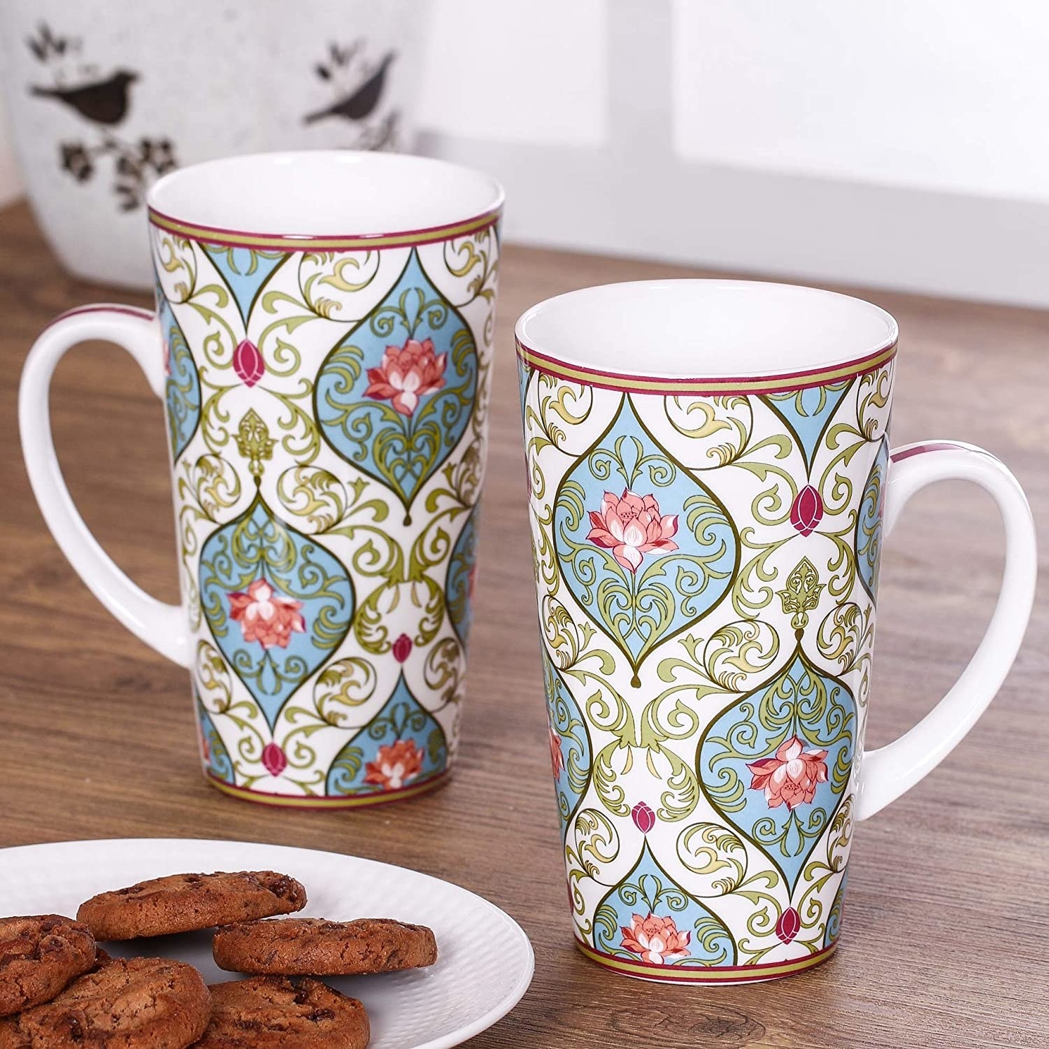 Two tall mugs next to chocolate chip cookies on a plate