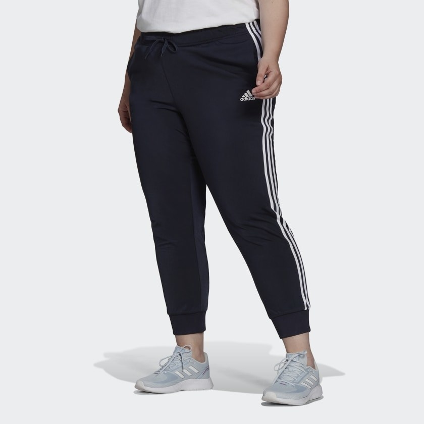 Model wearing black track pants with grey sneakers and a white top
