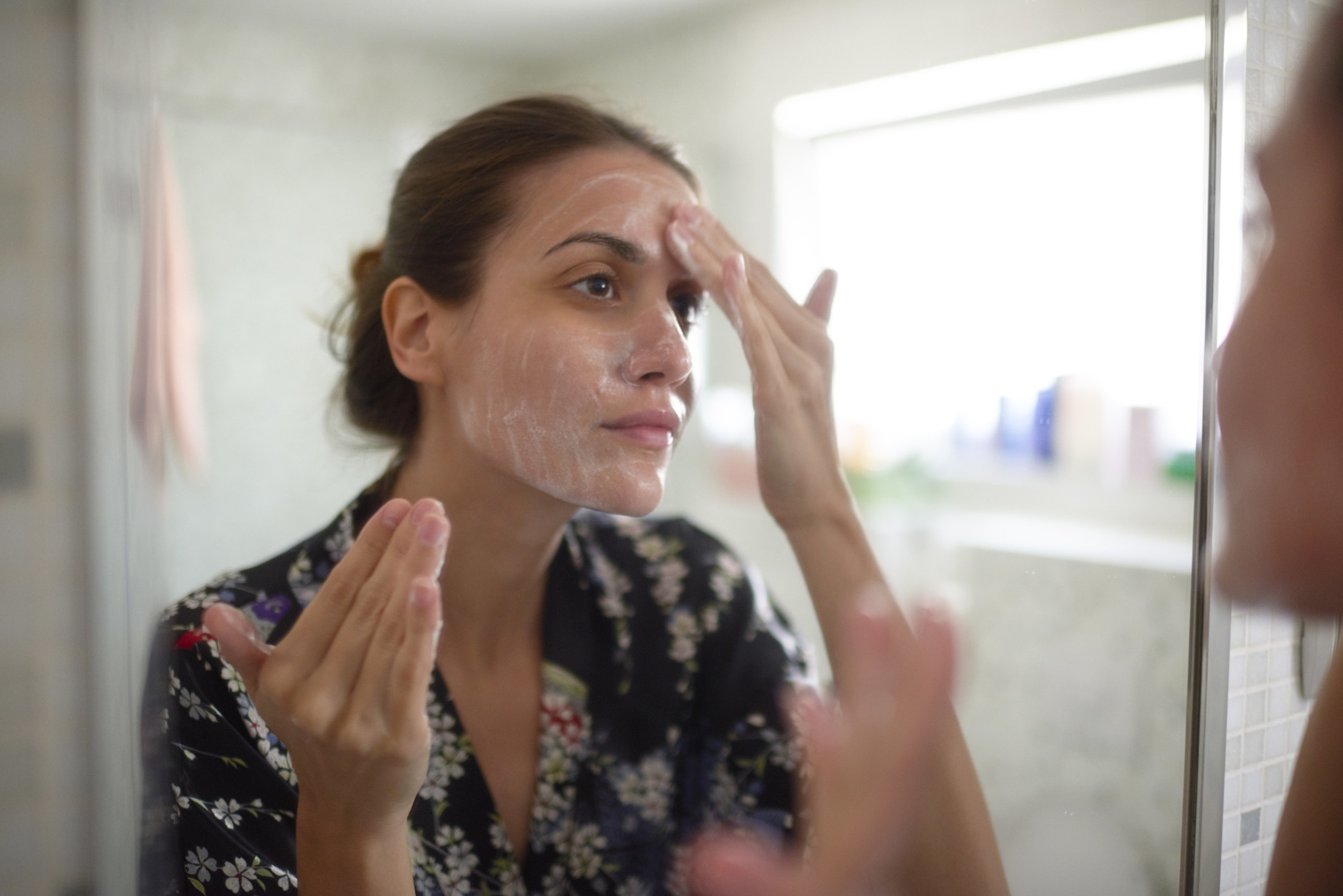 A woman washing her face and looking in the bathroom mirror