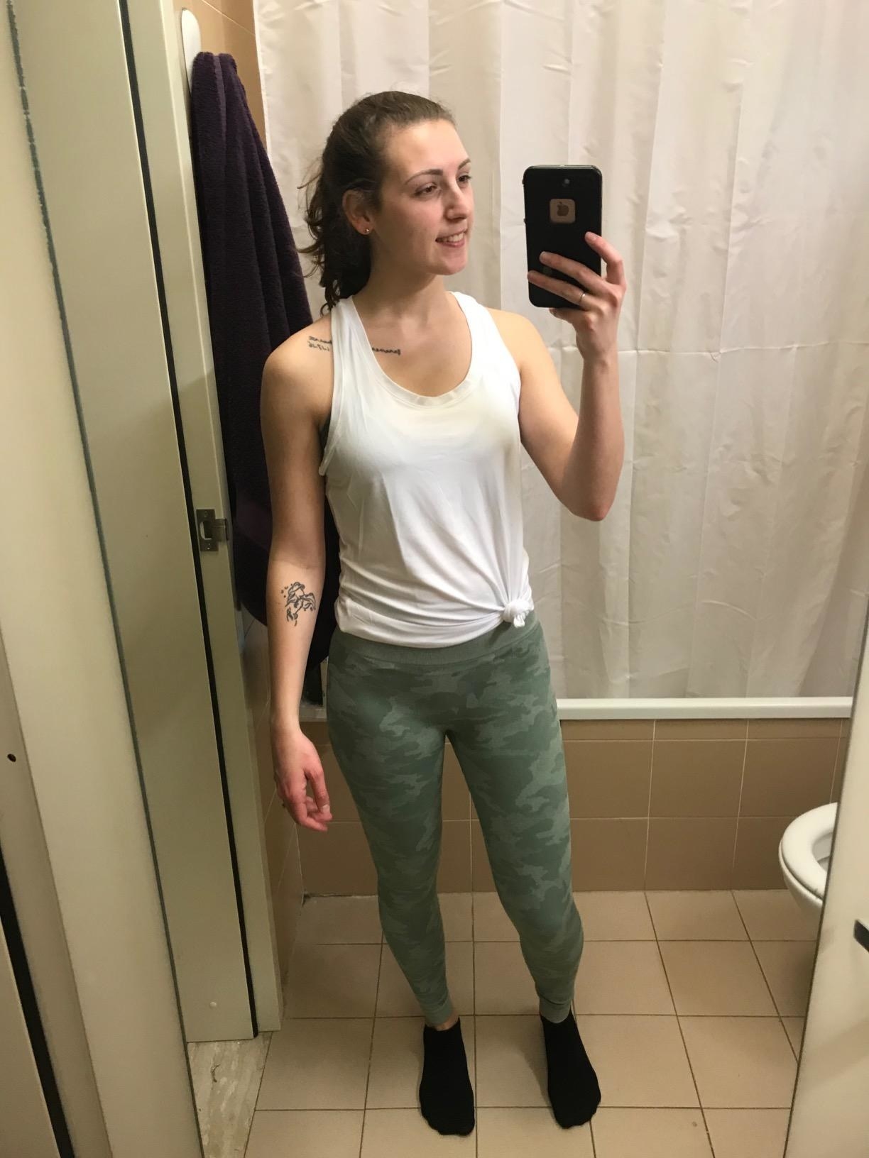 Reviewer is wearing a white tank and green camo leggings