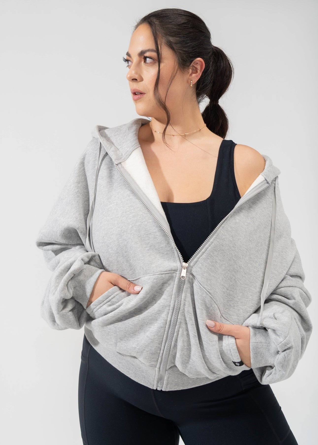 Model is wearing a light grey oversized hoodie with black leggings and a black sports bra