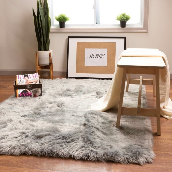 a fluffy gray area rug next to a stool and a black basket filled with magazines