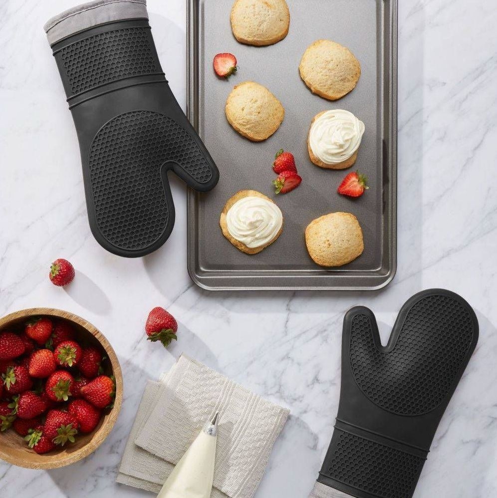 The two black oven mitts on a counter with a baking sheet