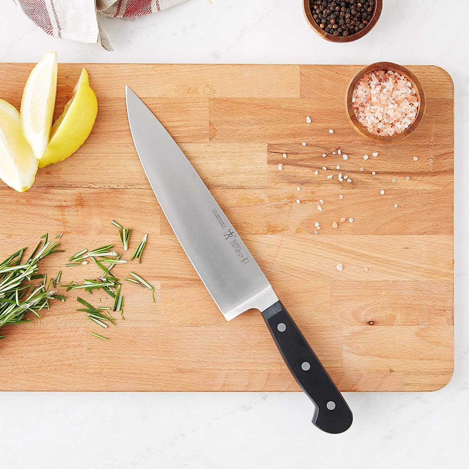 The knife on a cutting board next to lemon slices and rosemary